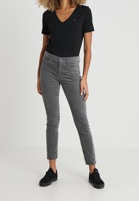 Graue Cordhosen mit schmaler Passform, ausgestattet mit fünf Taschen und feiner Struktur. Kombiniert mit einem eng anliegenden schwarzen V-Ausschnitt-T-Shirt und schwarzen Sneakers.