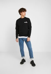Sudadera negra de manga larga con logo, combinada con vaqueros azules remangados y zapatillas negras. Diseño sencillo, material de algodón.