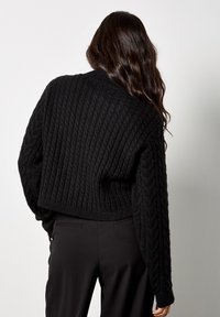 Czarny, dziany, krótký sweter z teksturowanym, prążkowanym wzorem i deseniem w warkocze. Posiada długie rękawy i okrągły dekolt.