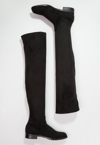 Botas negras por encima de la rodilla hechas de suave material de ante, con una superficie lisa, puntera redondeada, tacón bajo y sin herrajes visibles.