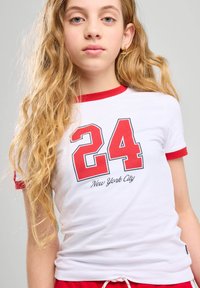 Camiseta blanca de manga corta con acentos en rojo, con el número "24" y "Nueva York" en script negro debajo del número.
