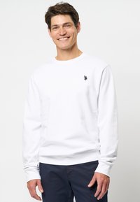 Witte sweatshirt van zachte stof, met een ronde halslijn, lange mouwen en een klein marineblauw logo op de borst.