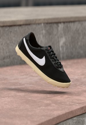 Schwarzer Mesh-Sportschuh mit weißem Nike-Swoosh, Schnürverschluss, leichtem Design und cremefarbener Gummisohle mit strukturiertem Grip.