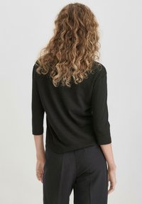 Schwarzes Dreiviertelarm-Oberteil, weiche Textur, lockere Passform, runder Ausschnitt, kombiniert mit maßgeschneiderten dunklen Hosen, minimalistisches Design.