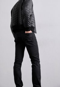 Black quilted leather bomber jacket with ribbed cuffs paired with fitted black pants featuring a pocket detail. Textured and sleek design.