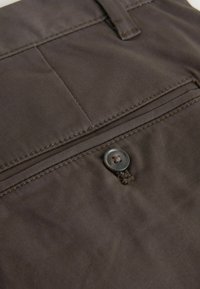 Tissu brun foncé en gros plan montrant une poche arrière boutonnée avec des coutures soignées et une passants de ceinture sur un pantalon.