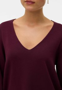 Maglione in maglia bordeaux con scollatura a V profonda e maniche lunghe. Tessuto morbido, vestibilità rilassata e design minimalista senza motivi o decorazioni.