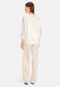 Silk blouse in off-white, featuring long, puffed sleeves and a square neckline, paired with light beige, wide-leg trousers.