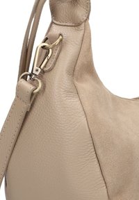 Beige leren en suède handtas met verstelbare schouderriem, metalen sluiting en ringbevestiging op een witte achtergrond.