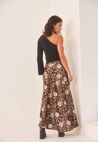 Top negro de un solo hombro combinado con una falda larga vaporosa marrón con un patrón que presenta acentos florales blancos y botas de plataforma negras hasta el tobillo.