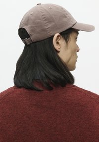 Bruine katoenen baseballcap met een verstelbare band aan de achterkant, voorzien van een gebogen rand en een gemêleerde stof. Draagt samen met een rode gebreide trui.
