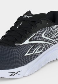 Μαύρο και γκρι καρό αθλητικό παπούτσι Reebok με λευκή σόλα, μαύρα κορδόνια και λευκό λογότυπο Reebok στο πλάι και στη γλώσσα.