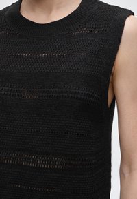 Αμάνικη μαύρη πλεκτή μπλούζα με εναλλασσόμενες οριζόντιες ρίγες από συμπαγές και διάτρητο ύφασμα, φορεμένη στον άνω κορμό ενός ατόμου.