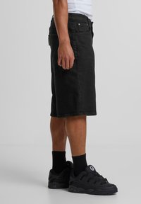 Shorts de mezclilla negra con un diseño de pierna recta, bolsillos laterales y detalles de costura sutiles, combinados con zapatillas negras y calcetines tobilleros.