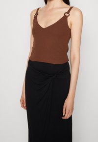 Brown ribbed tank top with V-neck and metal accent rings on straps, paired with a black wrap skirt featuring a knotted detail.