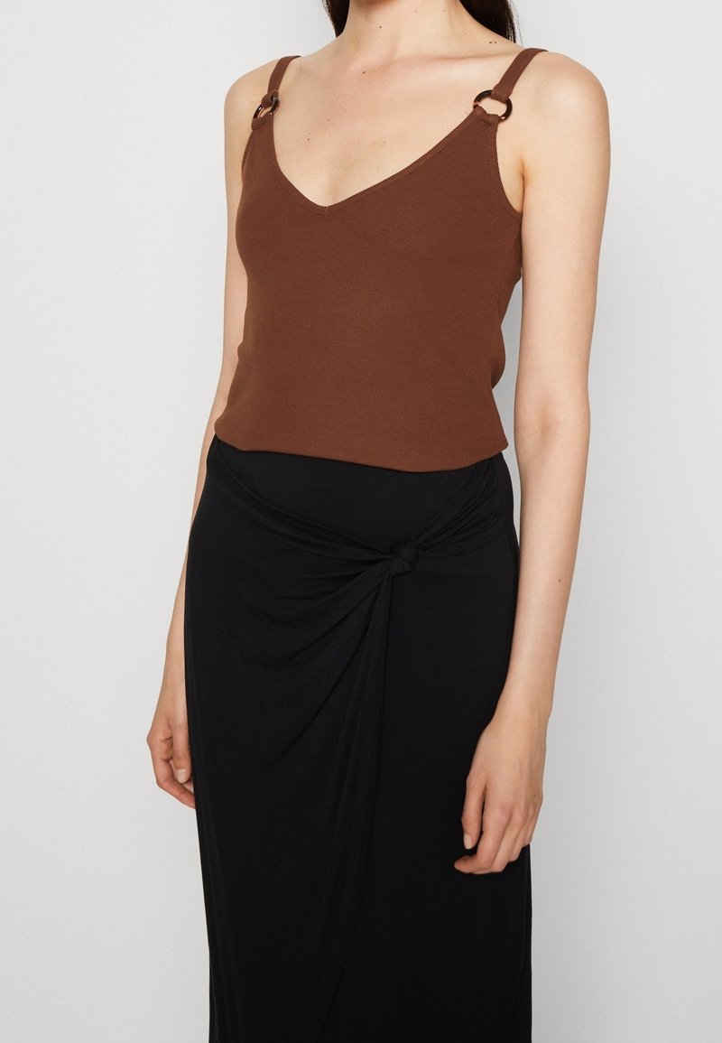 Brown ribbed tank top with V-neck and metal accent rings on straps, paired with a black wrap skirt featuring a knotted detail.