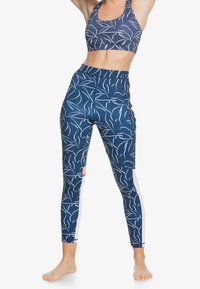 Mörkblå sport-bh och tights med vita bladmönster. Tightsen har en sidoficka och accentfärger i vitt. Slät, stretchig tyg.