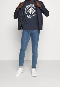 Navy t-shirt with white text, navy jacket, and blue skinny jeans. White sneakers complete the outfit, featuring a casual design.