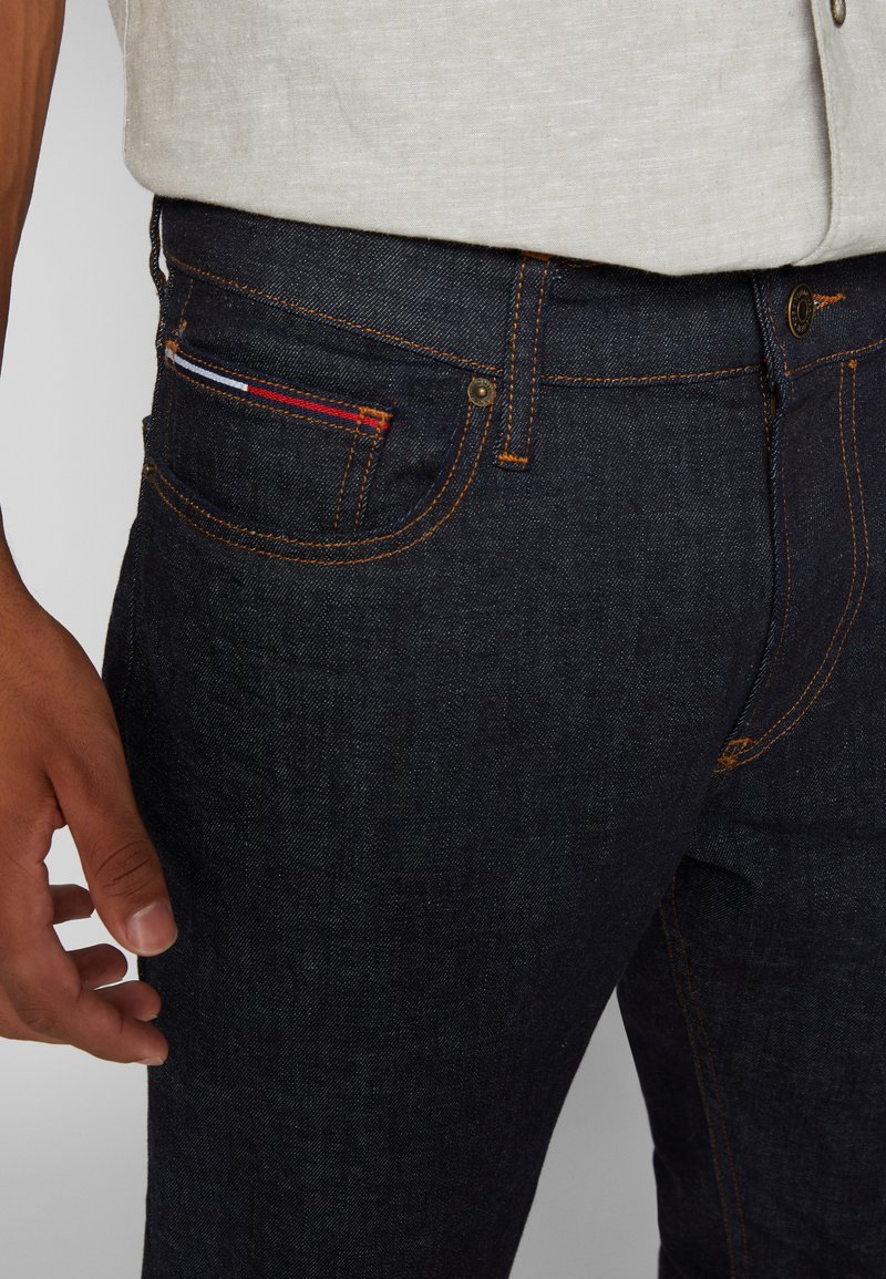Donkerblauwe denim jeans met oranje stiksels, een voorzak met een kleurrijke stofaccent en een aansluitende pasvorm.
