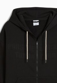 Sort zip-up hoodie med hvide snore, der har præget tekst "PORSCHE LEAGUE TURBO CLUB" på forsiden og en lomme foran.