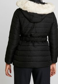 Černá prošívaná bunda s kapucí z umělé kožešiny. Má stahování v pase a vodorovný prošívaný vzor. Měkká textura, praktický design.