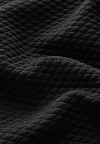 Tessuto nero trapuntato con un motivo a diamante, che presenta una texture morbida e una caduta fluida, ideale per applicazioni di abbigliamento o tappezzeria.