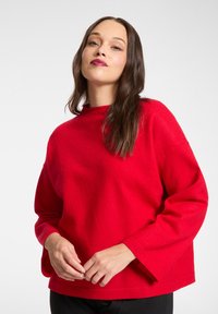 Roter Wollpullover mit hohem Ausschnitt, langen Ärmeln und lockerer Passform. Glatte Textur und schlichtes Design, geeignet für die Freizeit.