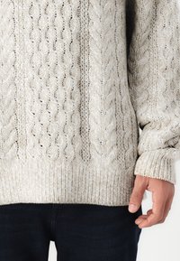 Κρέμα ζακέτα με πλέξη κασμίρ και υφή, με ριγωτούς μαντσέτες και στρίφωμα, κατασκευασμένη από μαλακό νήμα, συνδυασμένη με σκούρες τζιν παντελόνες.