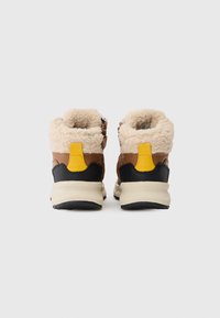 Een paar bruine winterlaarzen met beige fluffy voering, gele trekstropen, zwarte hakaccenten en dikke witte zolen, gezien vanuit de achterkant.