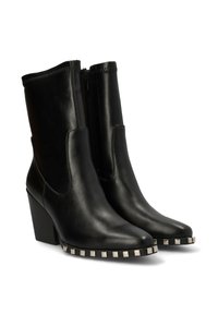 Botas de cuero negras hasta el tobillo con punta afilada, cierre de cremallera y tacón cuadrado. Presenta tachuelas metálicas a lo largo de la suela. Textura lisa.