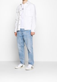 Chaqueta de mezclilla blanca sobre una camiseta blanca, combinada con jeans de color azul claro y zapatillas blancas con acentos verdes.