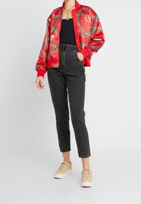 Röd satinbombarjacka med kedjemönster, svart åtsittande topp, högmidjade svarta jeans och beige sneakers med vita sulor.