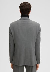 Giacca grigia con motivo strutturato, caratterizzata da un colletto nero e una silhouette strutturata. Vestibilità sartoriale con cuciture pulite e dettagli con bottoni.