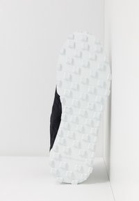 Baskets noires avec une tige texturée et une semelle extérieure en caoutchouc blanc dotée de crampons multidirectionnels pour une meilleure traction.