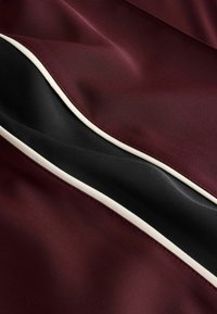 Bordo ir juodos audinio sluoksniai su lygiu paviršiumi, kuriuose išsiskiria kontrastinga balta apdaila aplink kraštus.