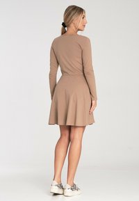 Beżowa sukienka z długim rękawem, dopasowanym gorsetem i rozkloszowanym dołem; wykonana z miękkiego materiału, posiada okrągły dekolt i elastyczny pasek w talii.