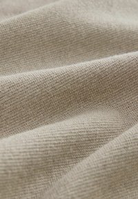 Gros plan d’un tissu tricoté beige montrant une texture fine et des plis doux.