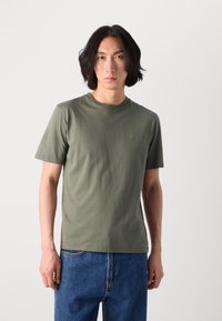 T-shirt en coton vert olive avec un col rond, des manches courtes et un logo brodé subtil sur la poitrine ; associé à un jean en denim bleu.