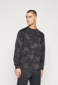 Long-sleeve black sweatshirt featuring a tie-dye pattern, round neckline, and soft fabric, worn with dark pants. Nike logo on the chest.