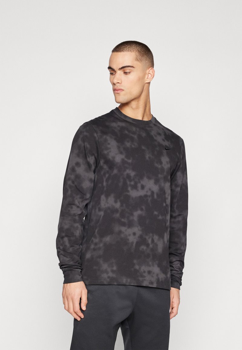 Long-sleeve black sweatshirt featuring a tie-dye pattern, round neckline, and soft fabric, worn with dark pants. Nike logo on the chest.