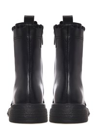 Paire de bottines en cuir noir avec semelles épaisses à nervures, fermeture éclair à l'arrière et languettes de tirage, vues de derrière sur un fond blanc.