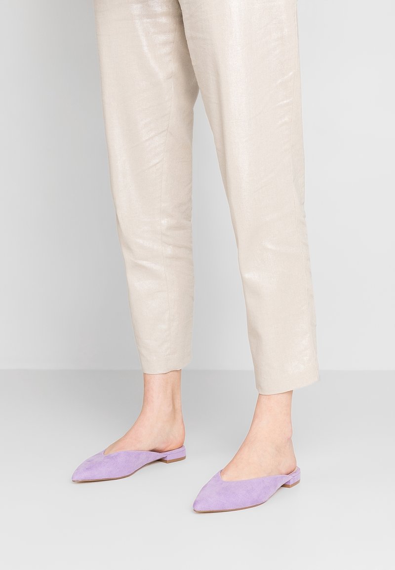 Mules en suede violet avec un bout pointu et un petit talon, associés à un pantalon tapered texturé beige clair.