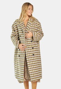 Przeciągający się, podwójnie zapinany płaszcz z wielokolorowej, teksturowanej wełny z domieszką, w kratę. Charakteryzuje się dużymi czarnymi guzikami i szerokimi klapami.