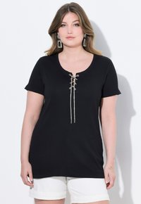 T-shirt nera a costine con maniche corte e scollatura a barca, con dettagli di lacci nella parte anteriore con accenti argentati. Abbinata a pantaloni corti bianchi.