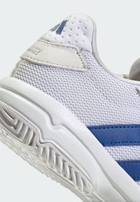 Baskets de sport blanches en mesh avec des rayures bleues, dotées d'une tige texturée, d'une semelle en caoutchouc lisse et d'un talon renforcé. Les accents incluent un patch avec logo.
