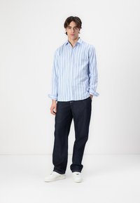 Hellblau gestreifte Button-Up-Bluse, die mit dunkelblauen Jeans und weißen Sneakers kombiniert ist. Die Bluse hat einen lässigen Schnitt und hochgekrempelte Ärmel.