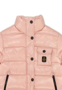 Giacca puffer rosa chiaro con colletto alto, bottoni a pressione, tasca frontale con patch logo e dettagli in cerniera nera. Tessuto liscio e trapuntato.
