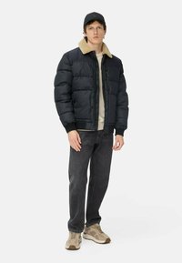 Polstret mørkegrå jakke med en beige fake fur krave, frontlynlås og strikkede manchetter, parret med mørke jeans og brune sneakers.