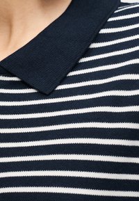 Ύφασμα με οριζόντιες ρίγες σε ναυτικό μπλε και λευκό, με υφασμένο γιακά σε ναυτικό μπλε, εμφανιζόμενο σε κοντινή λήψη.