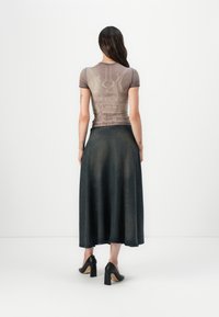 Tettsittende, gjennomsiktig brun topp med grafisk trykk, kombinert med et langt mørkt denimskjørt og svarte høye hæler, sett fra baksiden.